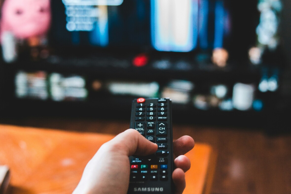 Henkilö osoittaa kaukosäätimellä televisiota.