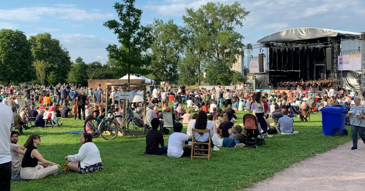 Kuvassa on käynnissä päivä konsertti. Ihmisiä istuu nurmikolla lavan edessä.