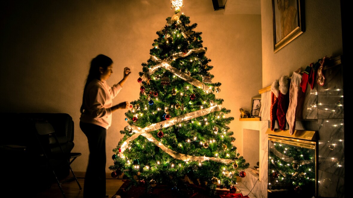 Lapsi koristelemassa joulukuusta hämärässä valaistuksessa