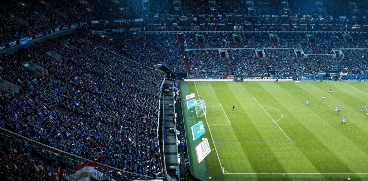 Jalkapallostadion näkyy osittain. Vasemmalla ja ylhäällä näkyy katsomo, joka on täynnä. Oikea reuna on jalkpallokenttä, jolla näkyy pelaajia. Kuva on otettu kaukaa.