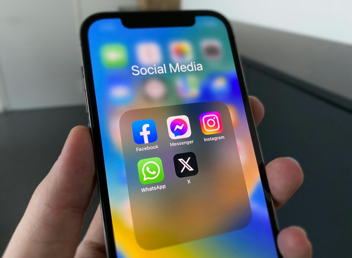 Kädessä on kännykkä. Puhelin on auki ja siinä näkyy erilaisten sovellusten ikonit. Sovellukset ovat järjestyksessä: Facebook, Messenger, Instagram, WhatsApp ja X.