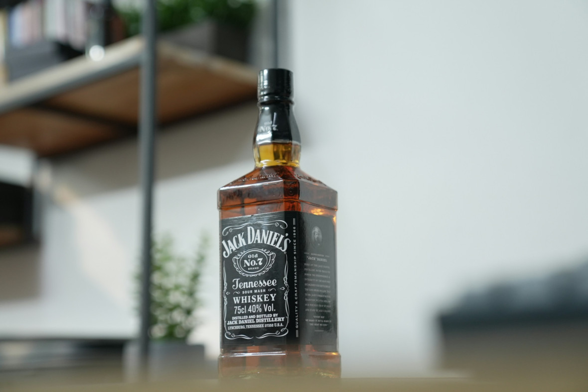 Hieman alakantista otettu kuva Jack Daniel's pullosta. Taustalla näkyy hylly ja kasvi.